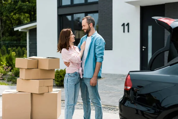 Femme heureuse debout avec homme barbu près de boîtes et nouvelle maison — Photo de stock
