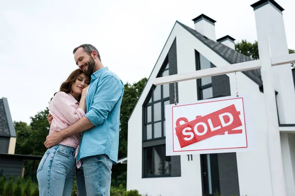 Счастливые мужчина и женщина обнимаются у борта с проданной арендой и домом — стоковое фото