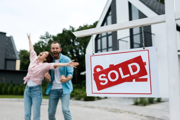 Selective focus of board with sold lettering near happy man gesturing with woman — Stock Photo