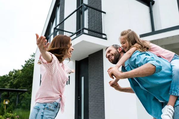 Visão de baixo ângulo da mulher com as mãos estendidas perto do homem piggybacking filha — Fotografia de Stock