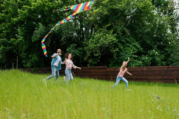 Happy kid running with colorful kite on green grass near parents — Stock Photo