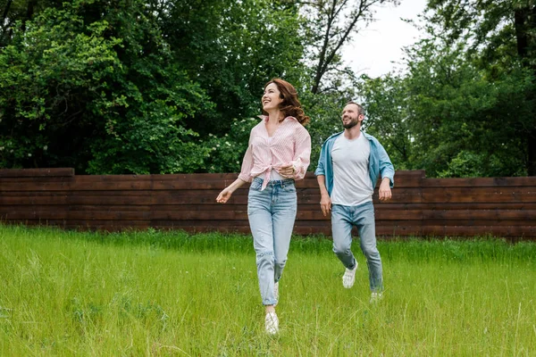 Heureux homme et femme courir sur l'herbe verte à l'extérieur — Photo de stock
