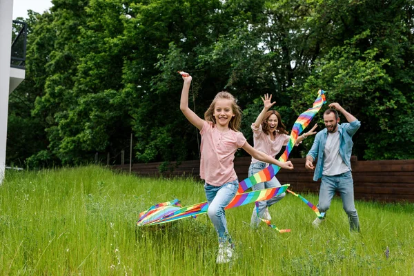 Glückliches Kind läuft mit buntem Drachen neben fröhlichen Eltern — Stockfoto