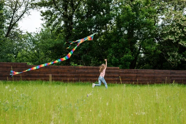 Selective focus of child running with colorful kite on green grass outside — Stock Photo