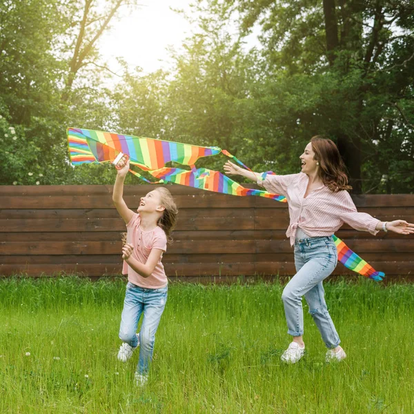 Glückliche Mutter mit ausgestreckten Händen neben niedlichem Kind mit buntem Drachen — Stockfoto