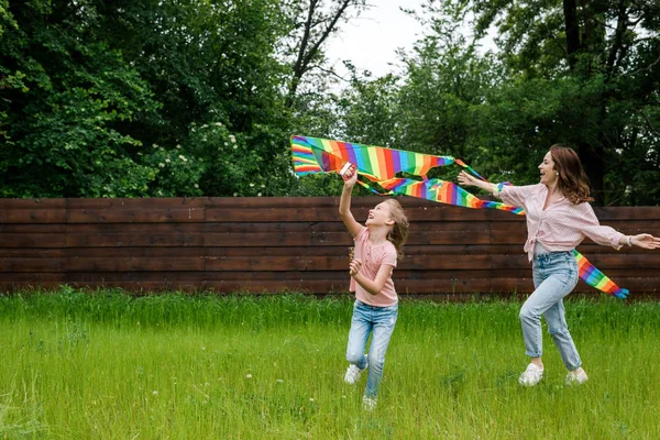 Allegra madre con le mani tese vicino al bambino carino con aquilone colorato — Foto stock