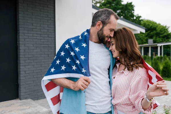 Happy bearded man standing with cheerful woman and holding american flag — Stock Photo