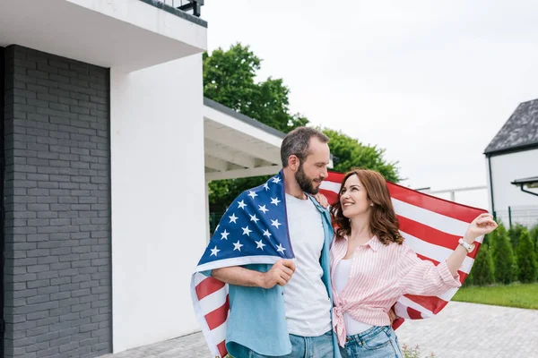 Happy bearded man standing with attractive woman and holding american flag — Stock Photo