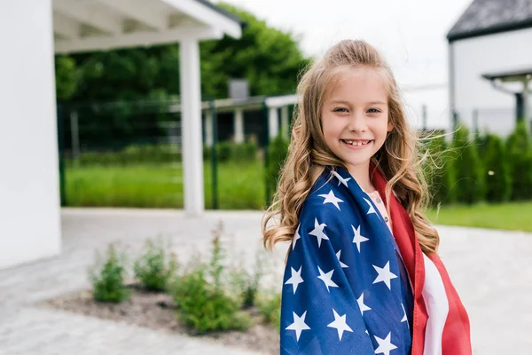 Criança alegre de pé com bandeira americana perto da casa — Fotografia de Stock