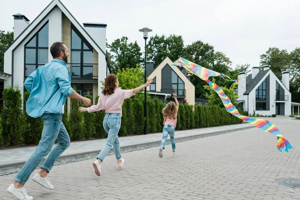 Visão traseira da criança correndo com pipa colorida perto dos pais na rua — Fotografia de Stock