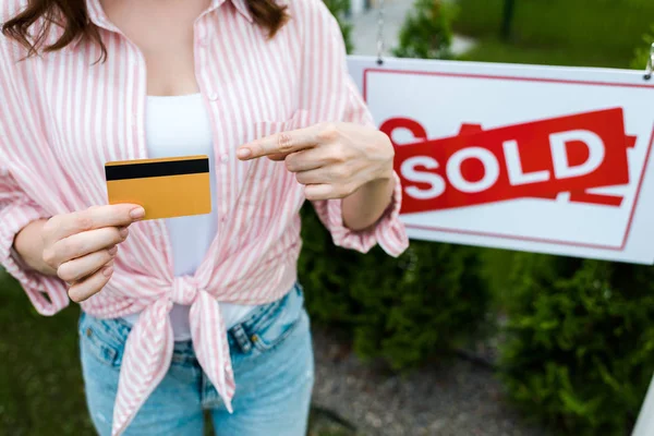 Cropped view of woman pointing with finger at credit card near board with sold letters — Stock Photo