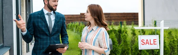 Panoramic shot of handsome bearded broker holding clipboard and gesturing near attractive woman — Stock Photo