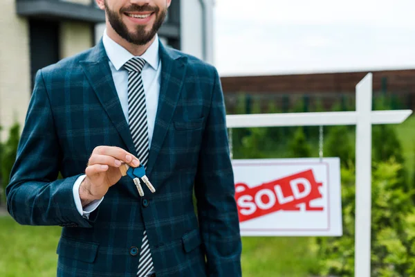 Обрізаний вид веселого брокера, що тримає ключі біля дошки з проданими літерами — стокове фото