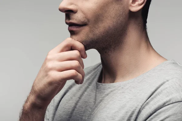 Visión parcial del hombre serio cogido de la mano cerca de la cara aislado en gris, emoción humana y concepto de expresión - foto de stock