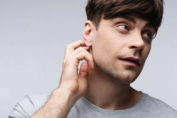 Hombre pensativo mirando hacia otro lado y tocando el cuello aislado en gris, emoción humana y concepto de expresión - foto de stock