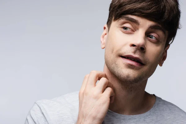 Sonriente hombre mirando hacia otro lado y sosteniendo la mano cerca del cuello aislado en gris, emoción humana y concepto de expresión - foto de stock