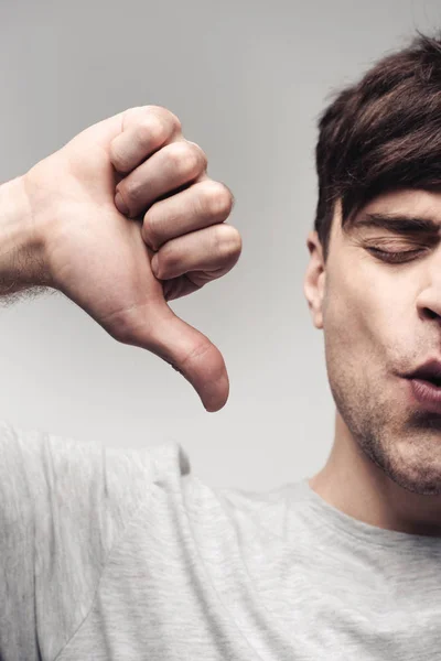 Hombre disgustado mostrando pulgar hacia arriba aislado en gris, emoción humana y concepto de expresión - foto de stock