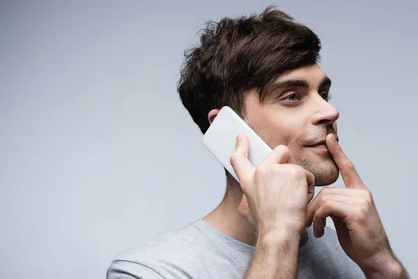 Sonriente hombre mostrando gesto de silencio mientras habla en el teléfono inteligente y mirando hacia otro lado aislado en gris - foto de stock