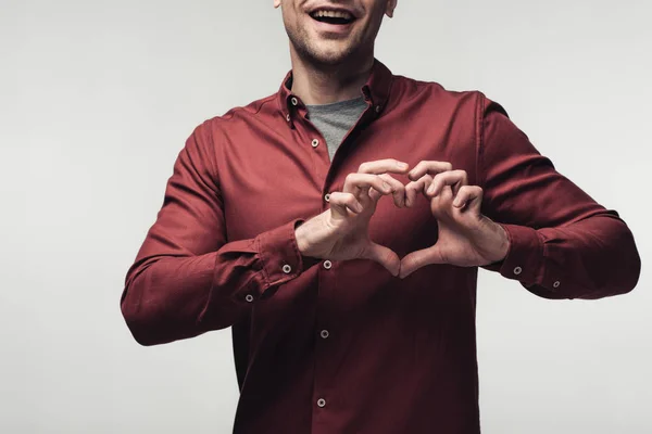 Teilansicht eines fröhlichen Mannes, der Herzzeichen zeigt, die Hände isoliert auf grauem, menschlichem Gefühl und Ausdruckskonzept — Stockfoto