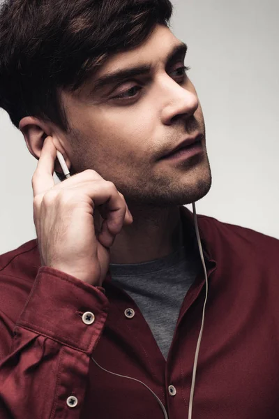 Hombre pensativo mirando hacia otro lado mientras escucha música en auriculares aislados en gris - foto de stock