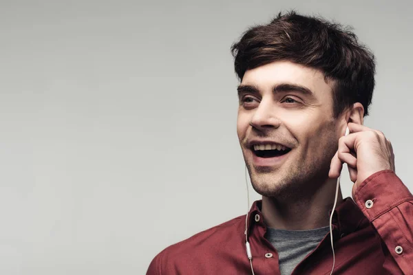 Cheerful young man looking away while listening music in earphones isolated on grey — Stock Photo