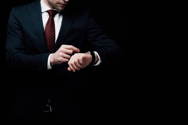 Vista parcial del hombre de negocios comprobar el tiempo de guardia aislado en negro - foto de stock