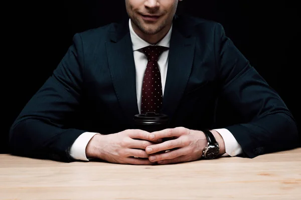 Homme d'affaires souriant assis au bureau et tenant du café pour aller isolé sur noir — Photo de stock