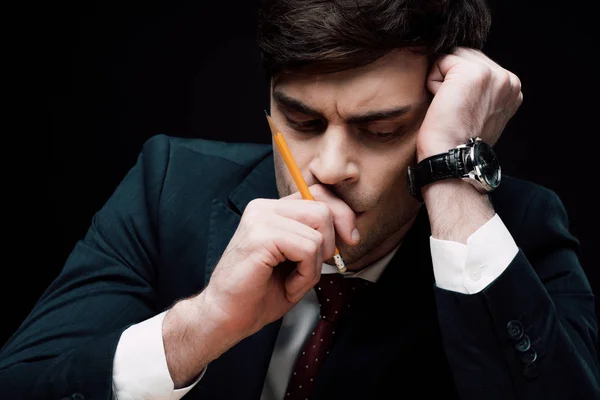 Upset, thoughtful businessman holding hand with pencil near face isolated on black — Stock Photo