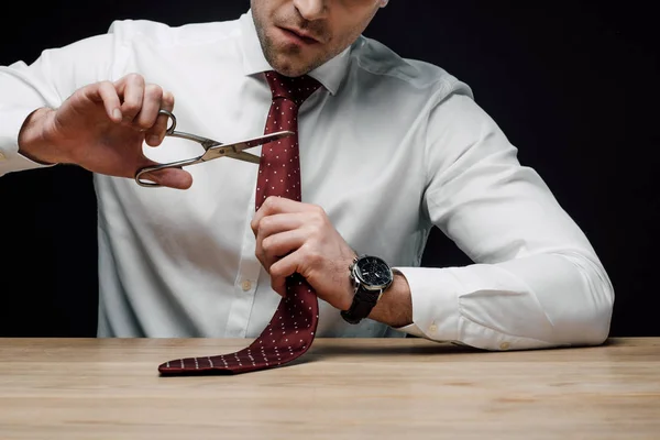 Turbato uomo d'affari taglio cravatta con forbici isolato su nero — Foto stock