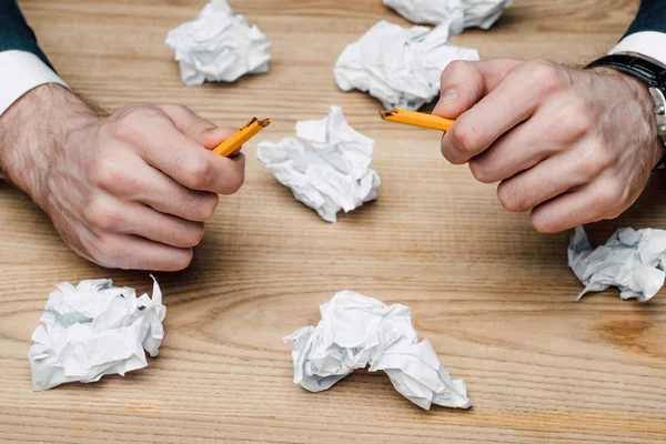 Cropped view of businessman holding broken pencil while sitting at wooden desk with crumpled pape — Stock Photo