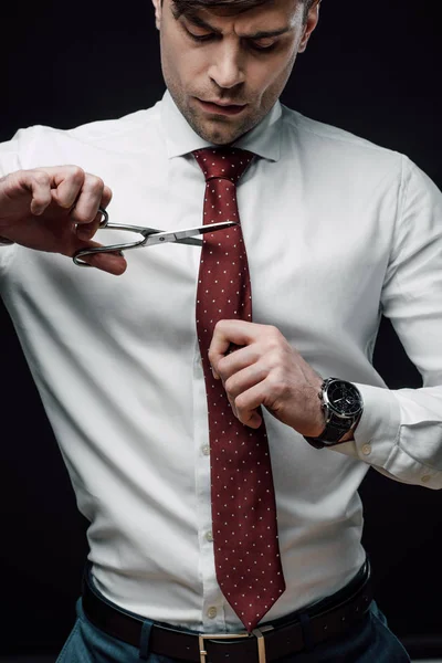 Molesto hombre de negocios cortando corbata con tijeras aisladas en negro - foto de stock