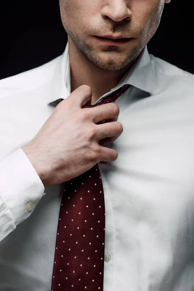 Partial view of serious businessman touching tie isolated on black — Stock Photo