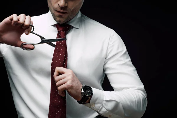 Vista ritagliata di deluso uomo d'affari taglio cravatta con forbici isolato su nero — Foto stock