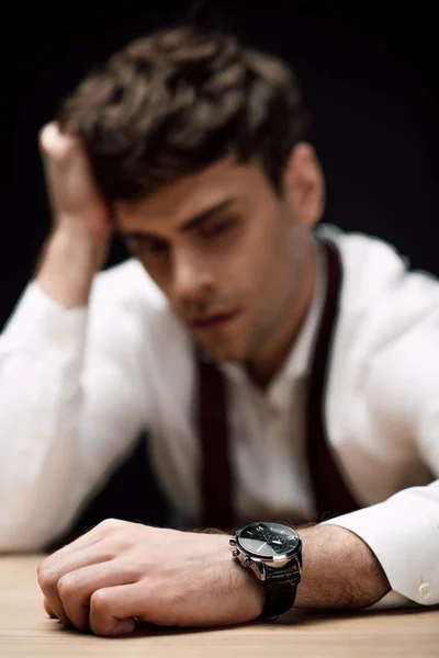 Selective focus of depressed businessman sitting at desk isolated on black — Stock Photo