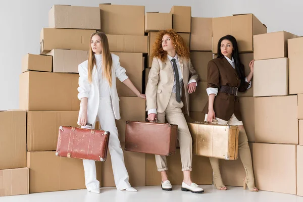 Multicultural girls standing with suitcases near boxes on white — Stock Photo