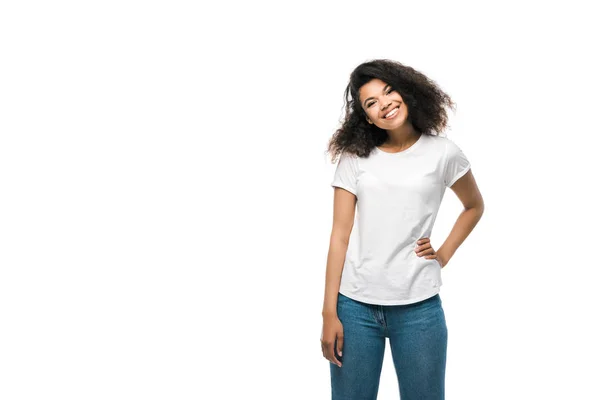 Chica afroamericana feliz en camiseta blanca de pie con la mano en la cadera aislado en blanco - foto de stock