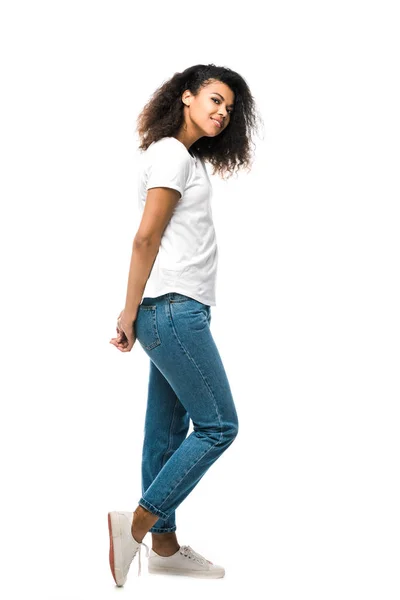 Счастливая африканская американка в белой футболке стоящая в синих джинсах изолированная на белом — стоковое фото