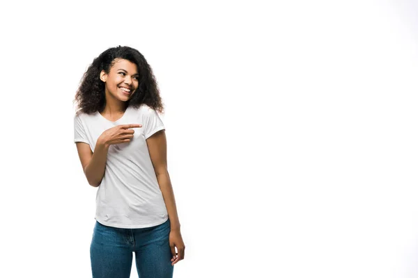 Happy african american girl in white t-shirt pointing with finger while standing in blue jeans isolated on white — Stock Photo