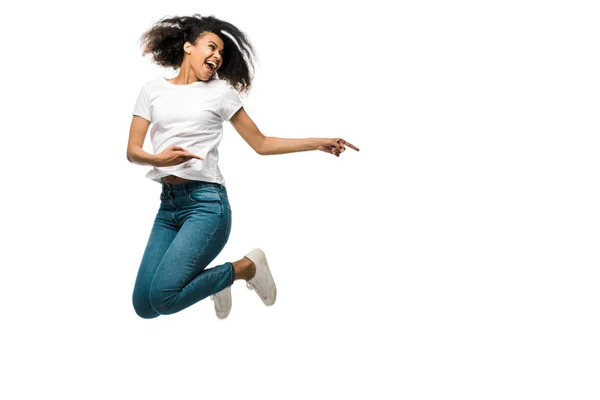 Femme afro-américaine souriante pointant des doigts et sautant isolé sur blanc — Photo de stock