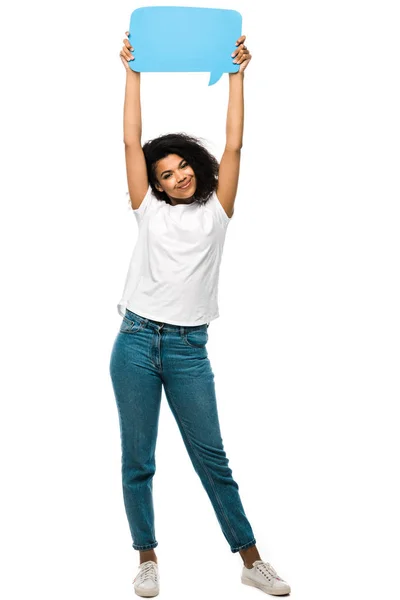 Happy african american girl holding blue speech bubble while standing in blue jeans isolated on white — Stock Photo