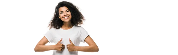 Панорамный снимок кудрявой и позитивной африканской женщины, показывающей большие пальцы на белом фоне — стоковое фото