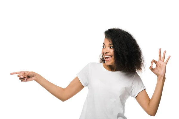 Веселый африканский американец женщина указывает пальцем, показывая ОК знак изолированы на белом — стоковое фото