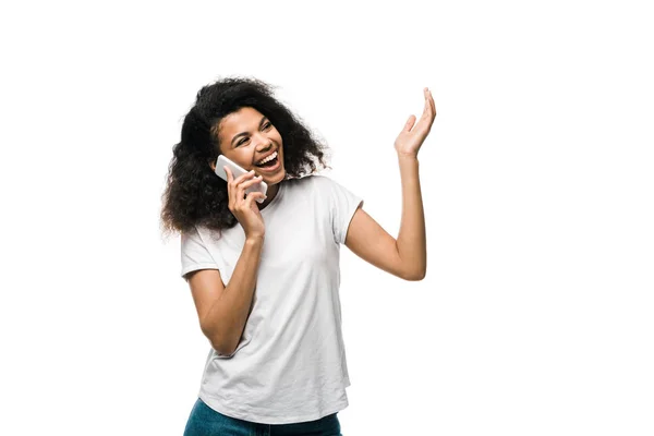 Alegre y rizado chica afroamericana hablando en el teléfono inteligente y el gesto aislado en blanco - foto de stock