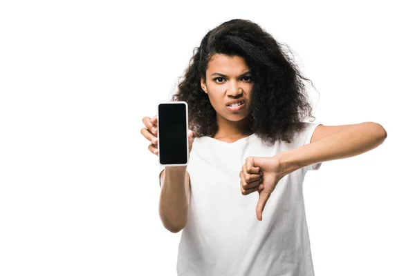 Niña afroamericana disgustada sosteniendo teléfono inteligente con pantalla en blanco y mostrando el pulgar hacia abajo aislado en blanco - foto de stock