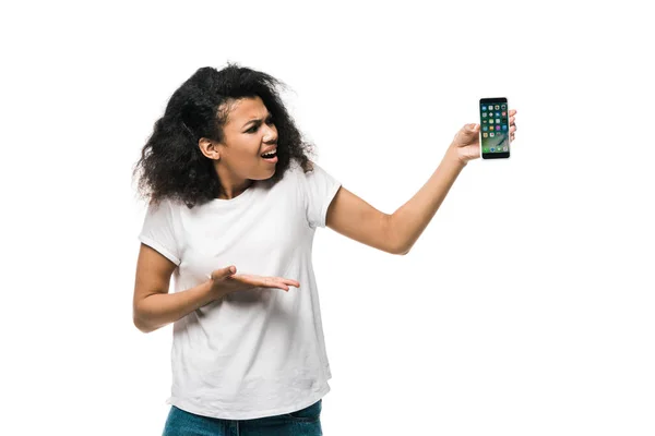 KYIV, UCRANIA - 29 de mayo de 2019: niña afroamericana disgustada haciendo gestos mientras sostiene el iphone aislado en blanco - foto de stock