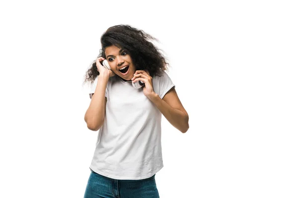 Chica afroamericana sorprendida sosteniendo auriculares mientras escucha música aislada en blanco - foto de stock