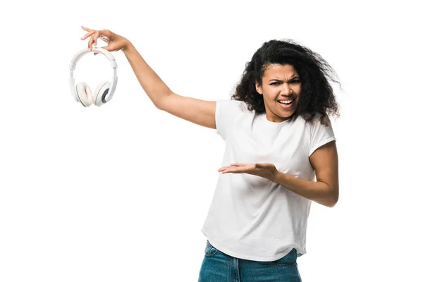 Desagradado afro-americano encaracolado homem gesticular enquanto segurando fones de ouvido isolados em branco — Fotografia de Stock