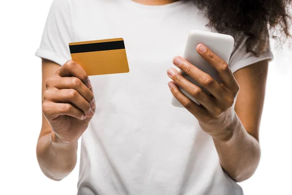 Обрізаний вид афроамериканської жінки, що тримає кредитну картку біля смартфона ізольовано на білому — стокове фото