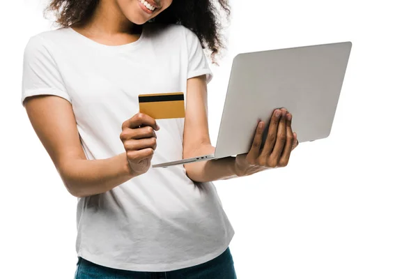 Обрізаний вид веселої афроамериканки, що тримає кредитну картку біля ноутбука ізольовано на білому — стокове фото
