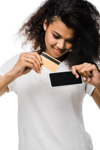 Glücklich afrikanisch-amerikanische Frau hält Kreditkarte in der Nähe Smartphone mit leerem Bildschirm isoliert auf weiß — Stockfoto